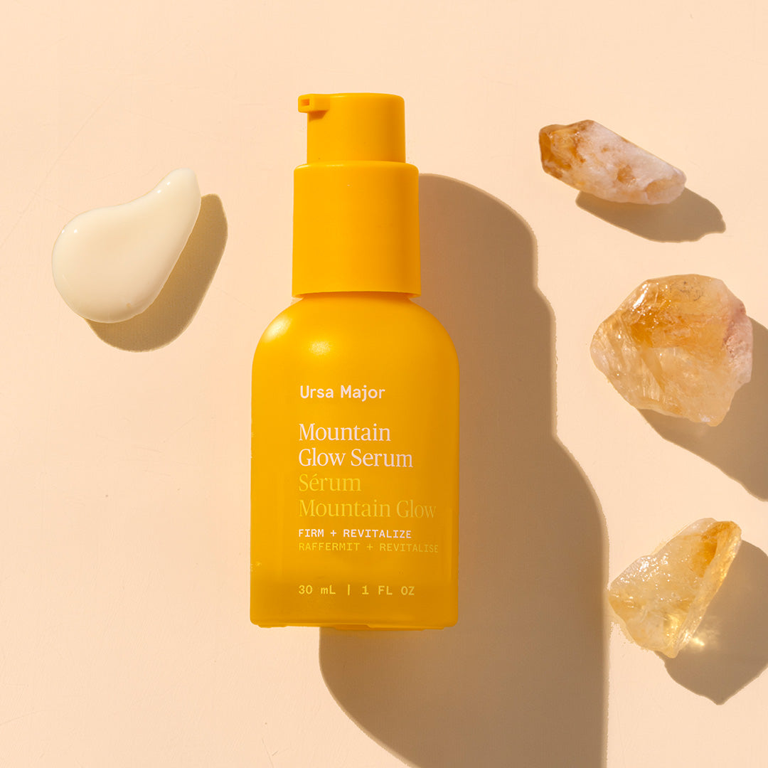 Ursa Major | Mountain Glow Serum | Styled image with swatch - yellow product bottle laying on each background with product swatch