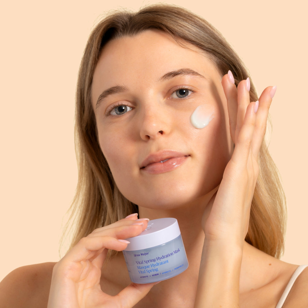 Ursa Major | Vital Spring Hydration Mask | Model Image - woman applying mask to cheek while holding the jar against a neutral background