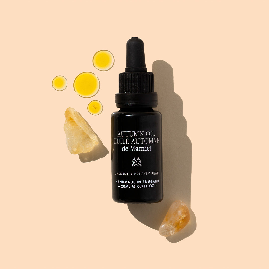 de Mamiel | Autumn Facial Oil | Styled Image with Swatch_Sep26 - black dropper bottle with oil swatches and crystals on a peach background
