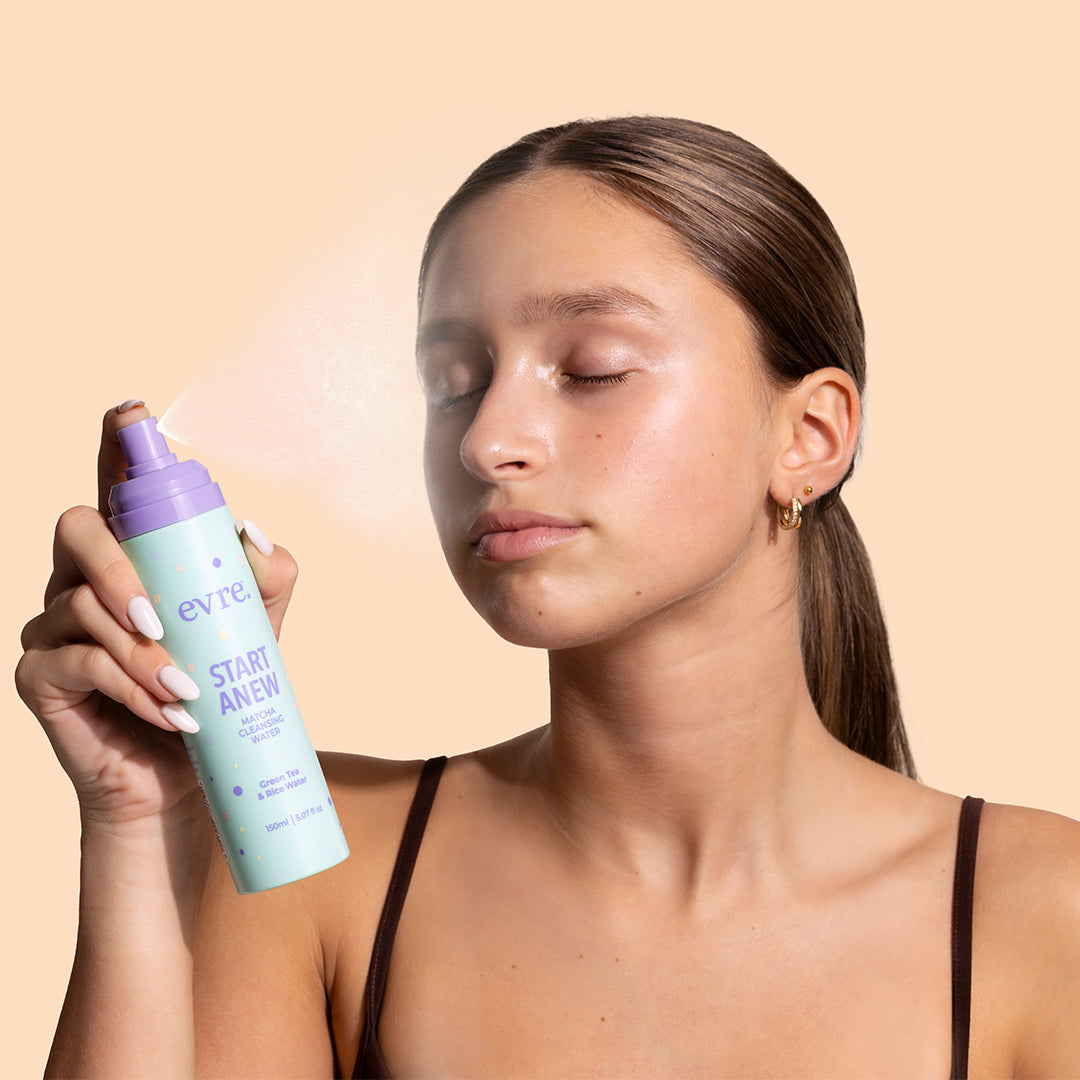 evre. | Start Anew Matcha Cleansing Water | Model Image - model misting cleansing water onto her face against a peach background