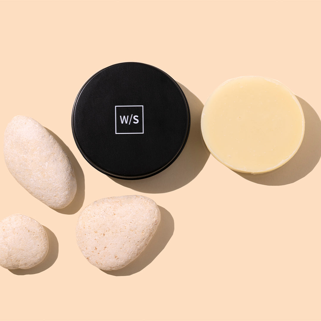 withSimplicity | Brush Cleansing Balm | Styled Image_Sep26.jpg - brush cleansing balm in black jar with pale yellow balm on peach background with white stones