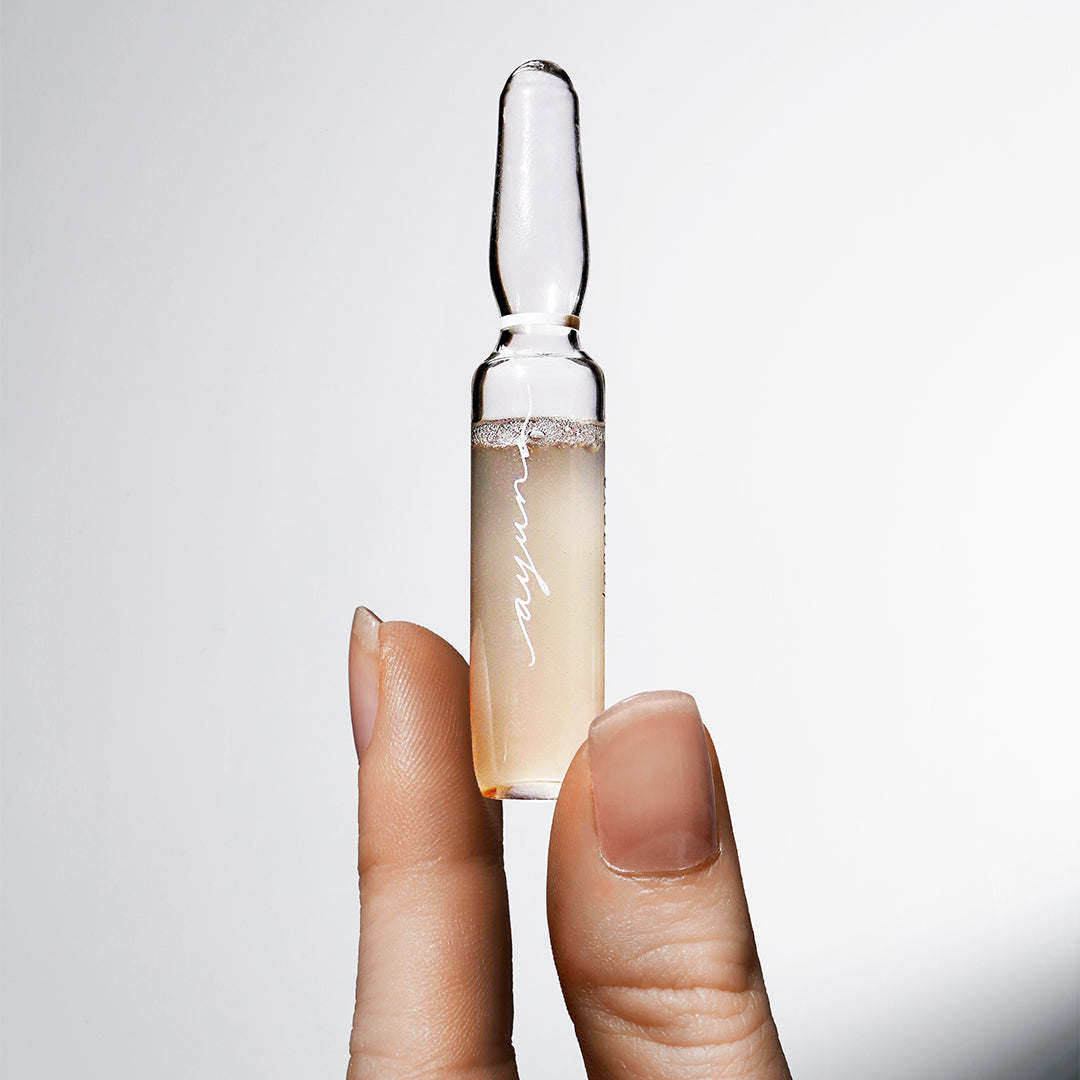 AYUNA | Longeva | Close-up Product Image - hand holding ampoule against a soft gray background
