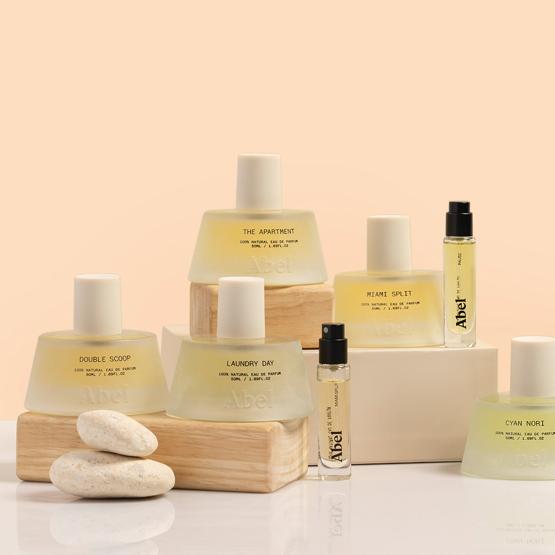Abel | Eau de Parfum Group Image | Full and Travel Size | Group image of fragrance bottles both 50 ml and 6 ml, frosted glass sitting on wooden blocks