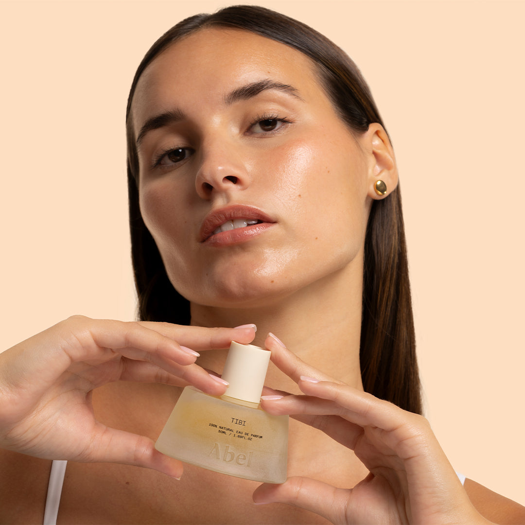 Abel | Tibi | Model Image_Oct26 - Model holding perfume bottle against a peach background