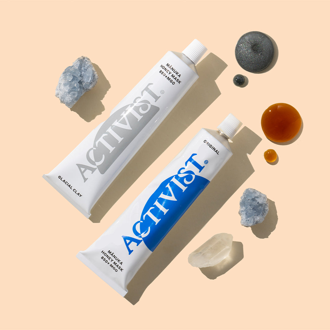 Activist | Mānuka Honey Glacial Clay Mask and Mānuka Honey Mask 850+ MGO | Styled Image with Swatch_Sep26 - two white honey mask tubes with gray and blue labels, surrounded by crystals and product swatches on a peach background