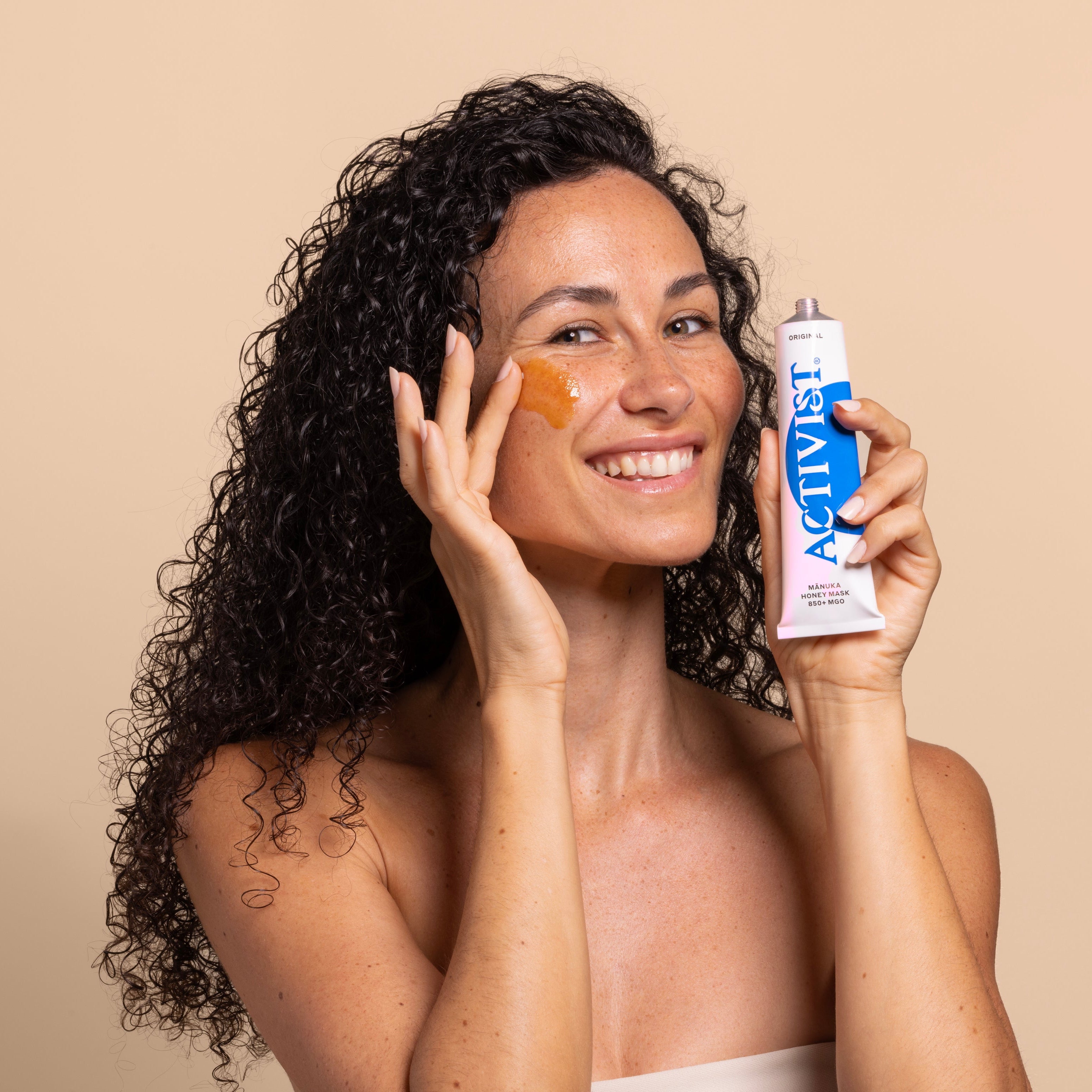 Activist Manuka Honey Mask - female model holding tube against beige background