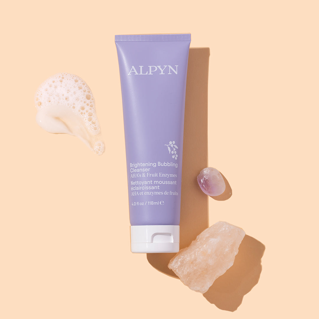 Alpyn Beauty | Brightening Bubbling Cleanser | Styled Image with Swatch - bubbling cleanser tube styled with foam, crystal, and stone on a beige background
