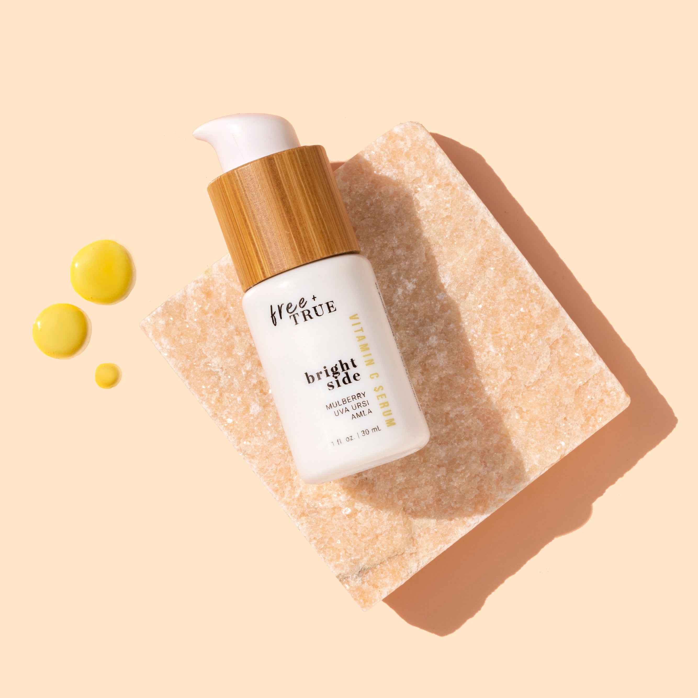 Free + True | Bright Side | Styled image with swatch | white bottle on peach background with yellow product swatch 