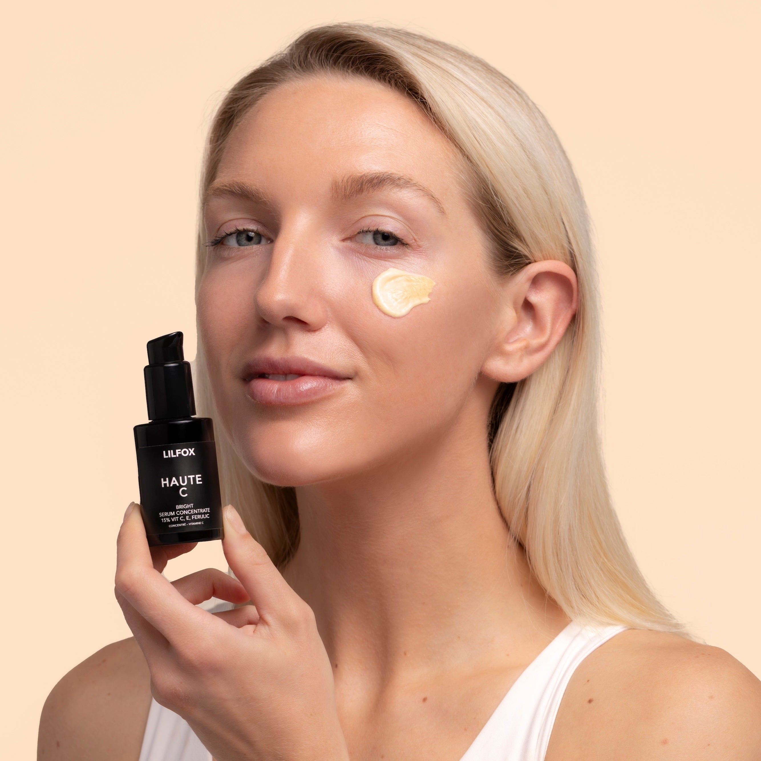 LILFOX Haute C, model on peach background holding black  bottle with product swatch near face