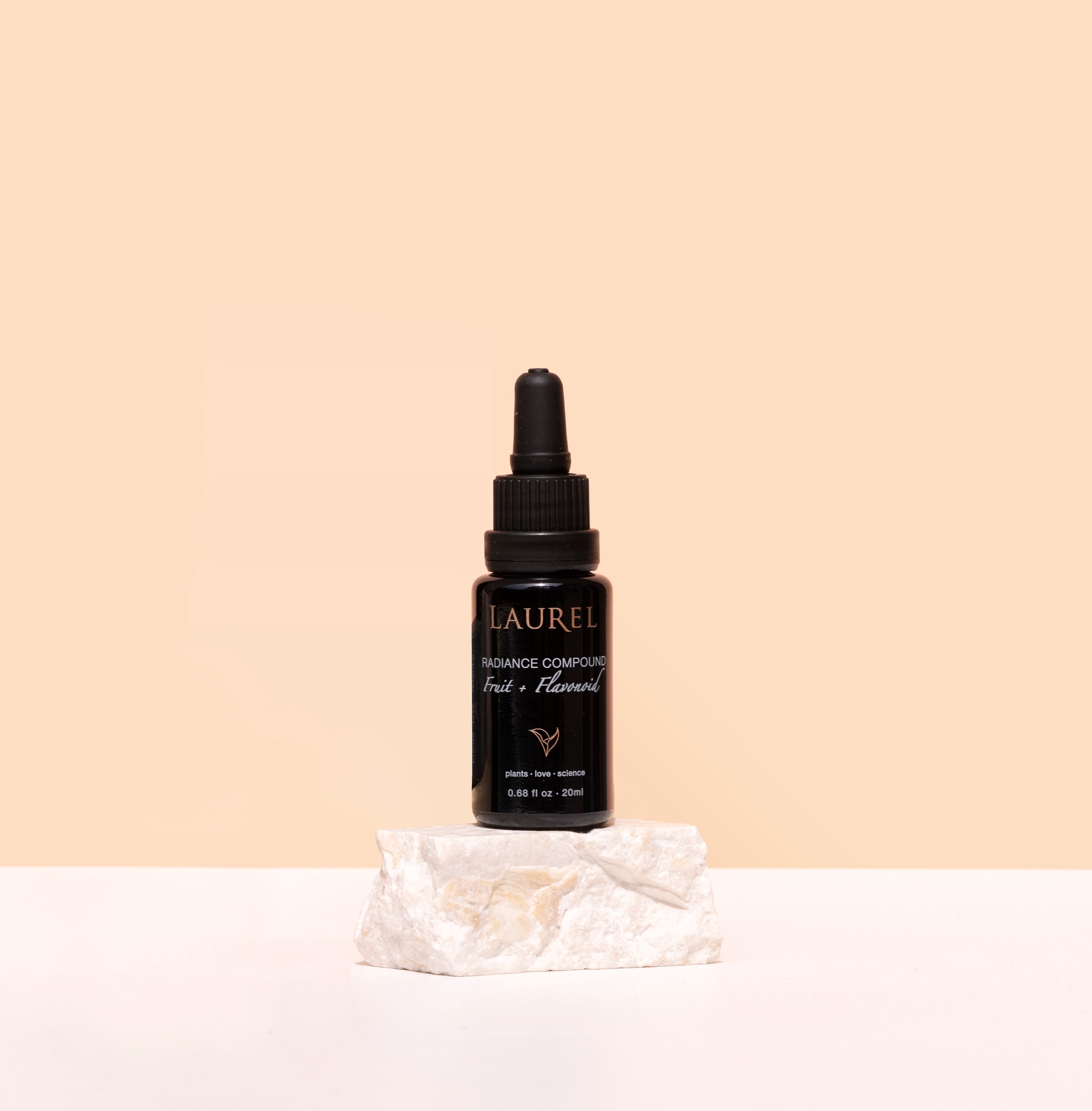 Laurel Skin | Radiance Compound | Styled Image | Black bottle with dropper on white stone, beige background