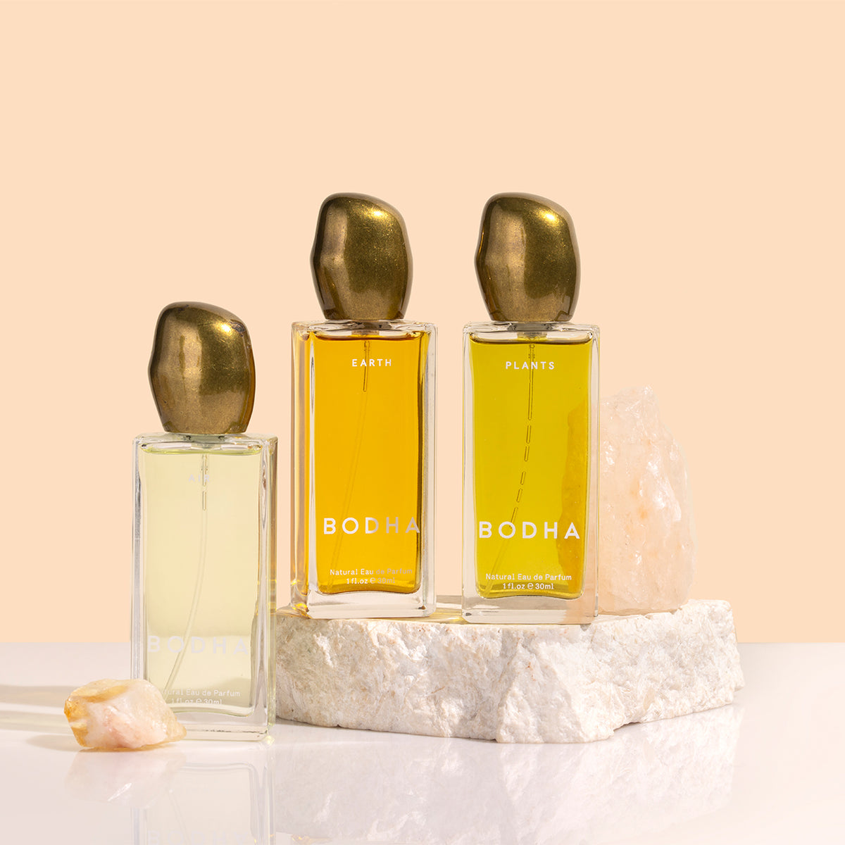 BODHA | Elemental Eau de Parfum | Styled Image_Nov26 - three BODHA Eau de Parfum bottles in Air, Earth, and Plants displayed with natural stones against a peach background