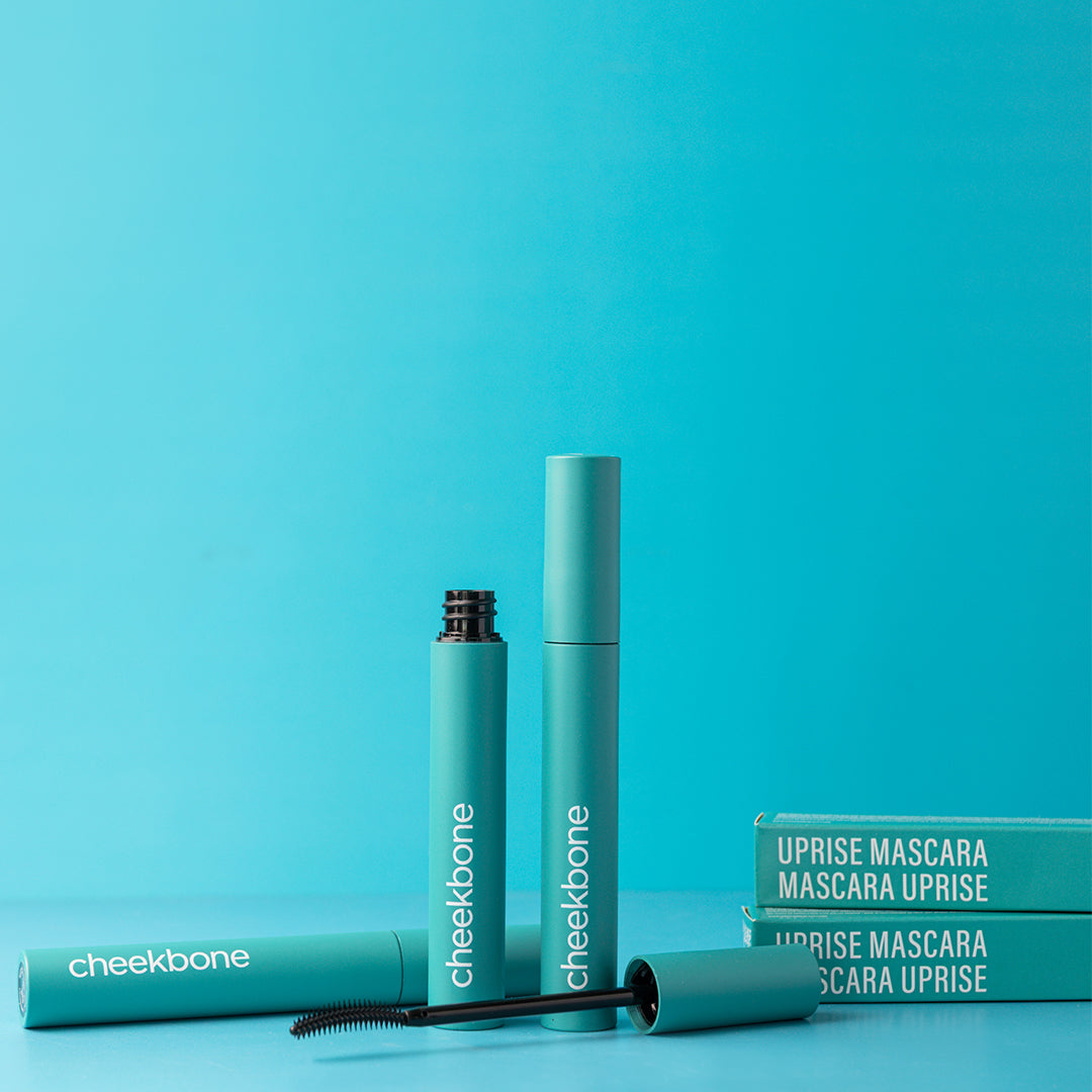 Cheekbone Beauty | Uprise Mascara | Flatlay Image - mascara tubes, wand, and product boxes styled on a turquoise blue background