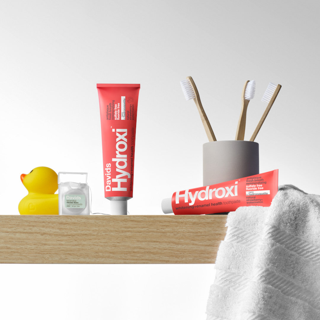 Davids | Hydroxi™ Kids + Adults Toothpaste - Strawberry + Watermelon | Product Image - red toothpaste tube with minimal bathroom accessories