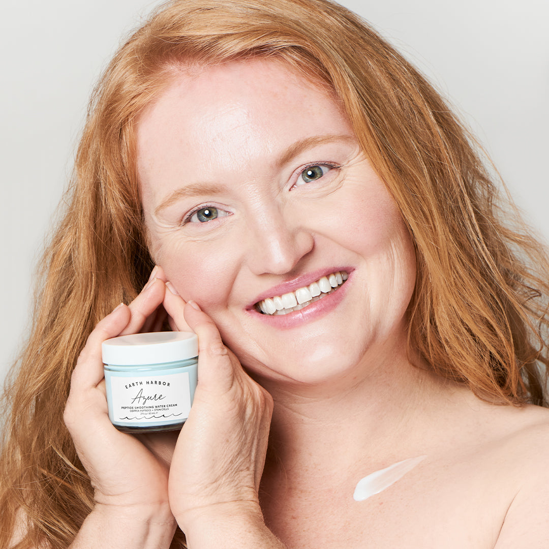 Earth Harbor | Azure Peptide Smoothing Water Cream | Model Image - smiling woman holding jar beside her face with a cream swatch on her shoulder