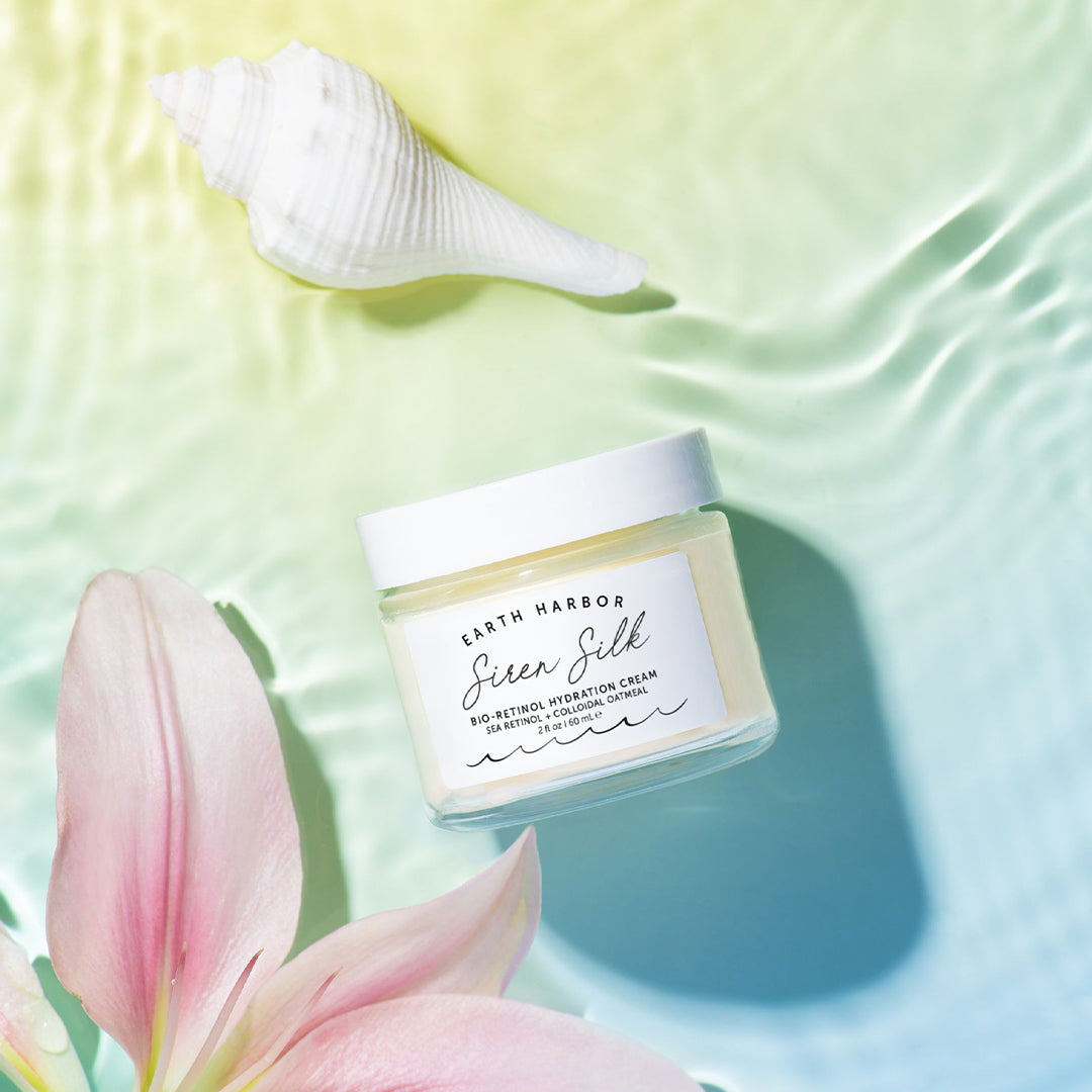 Earth Harbor | Siren Silk Bio-Retinol Hydration Cream | Lifestyle Image - cream jar displayed with a white seashell and pink flower on a pastel background