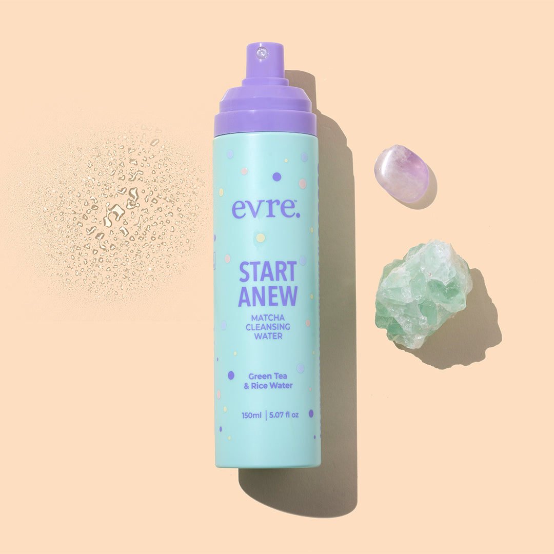 Evre. | Start Anew Matcha Cleansing Water | Styled Image with Swatch_Sep26 - bottle with lavender pump on a peach background, surrounded by water droplets and colorful crystals