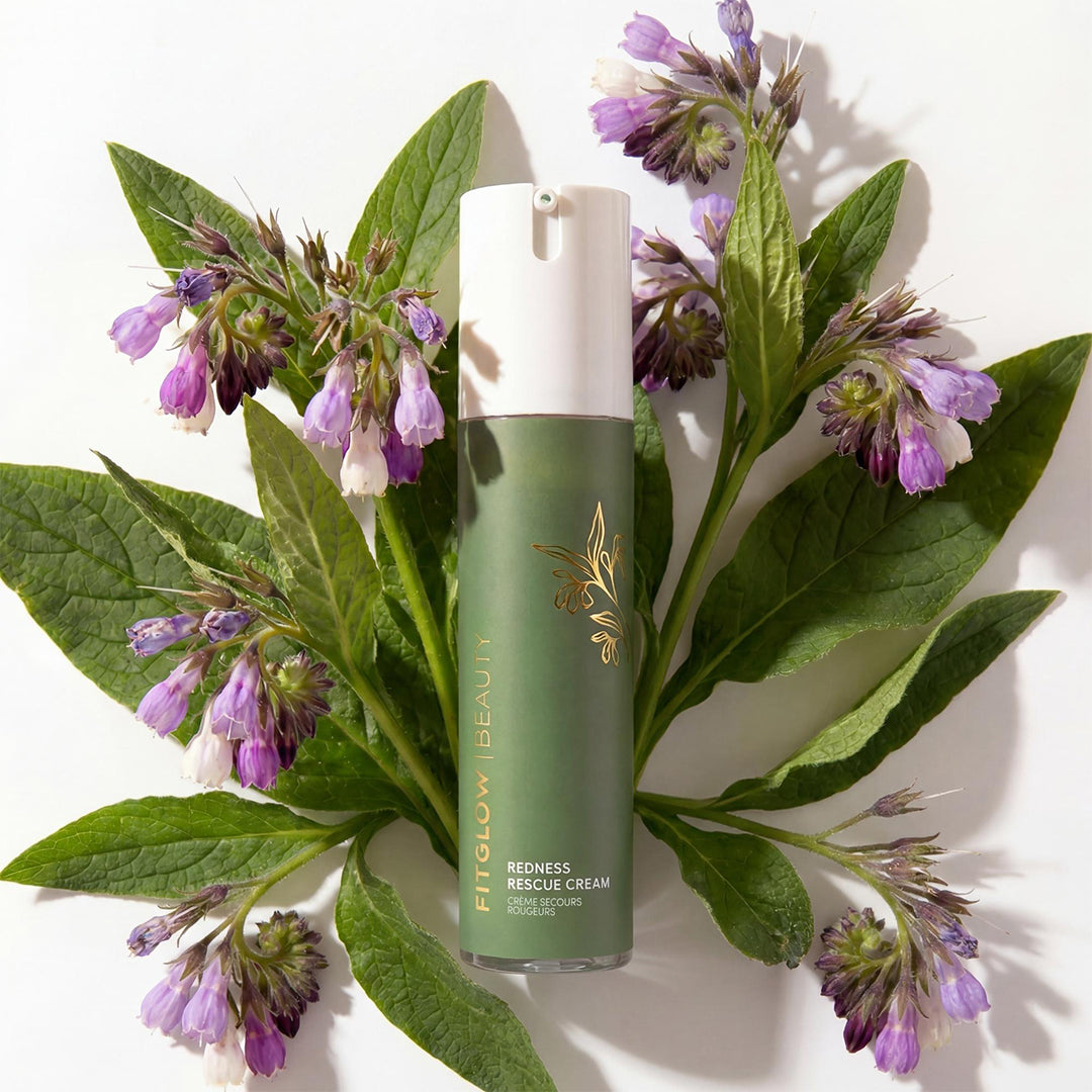 Fitglow Beauty | Redness Rescue Cream | Lifestyle Image - green bottle surrounded by green leaves and purple flowers on a white background