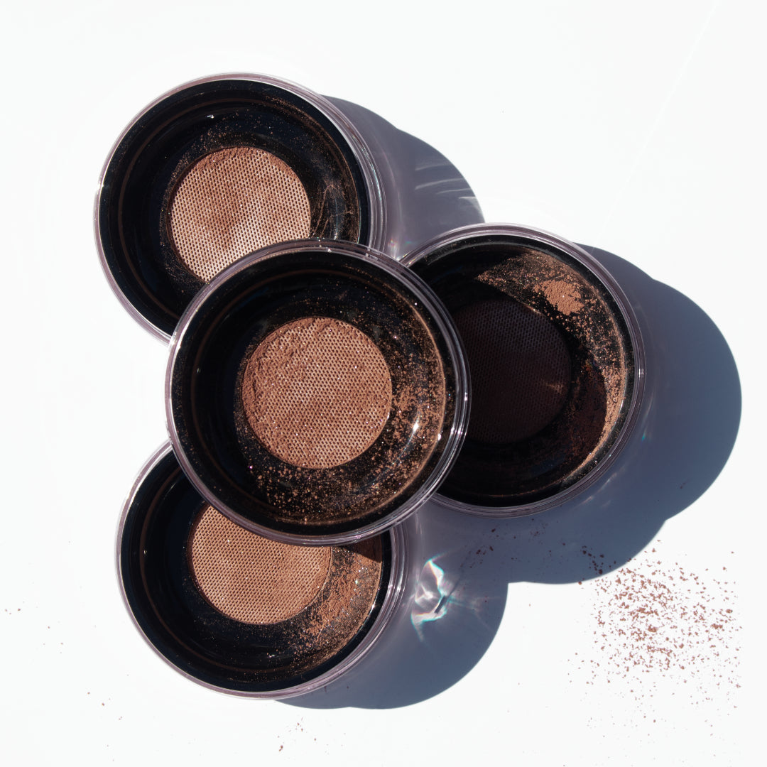 Fitglow Beauty | Vita Illuminate + Bronze Loose Powder | Flatlay Product Image - four open jars of loose mineral powder makeup arranged on a white surface with scattered powder