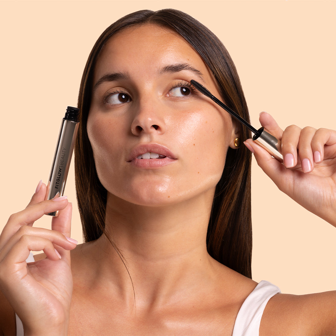 Fitglow | Lash Care Mascara | Model Image_Oct26 - metallic silver tube with a black mascara wand against a warm peach background