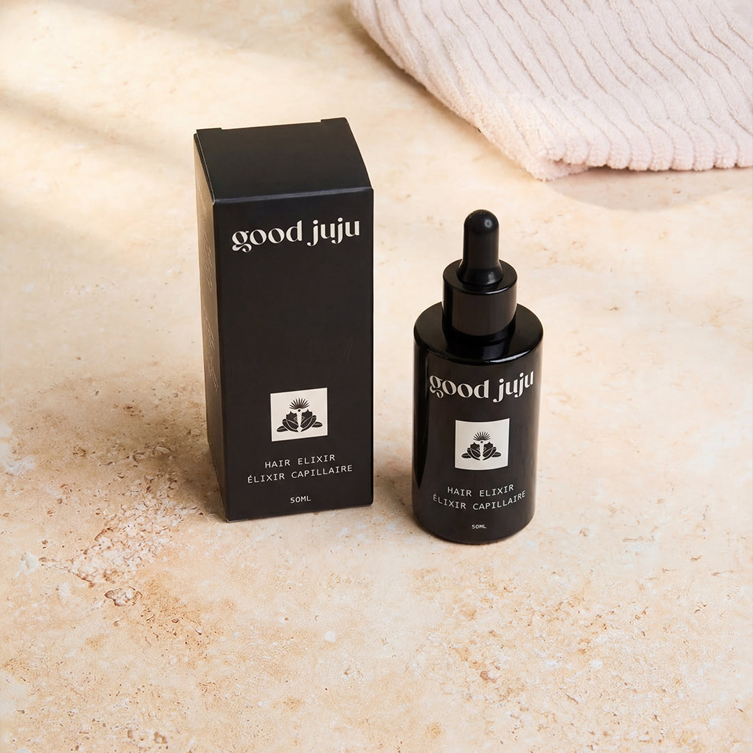 Good Juju | Hair Elixir | Bottle and Box Display - bottle with dropper beside its black product box on a beige stone surface