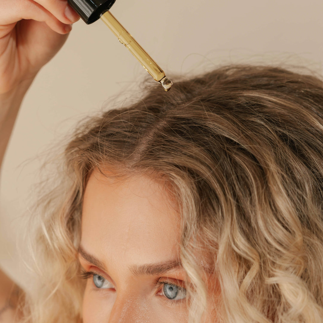 Good Juju | Hair Elixir | Model Image with Swatch - person applying elixir to the scalp with a glass dropper over wavy hair