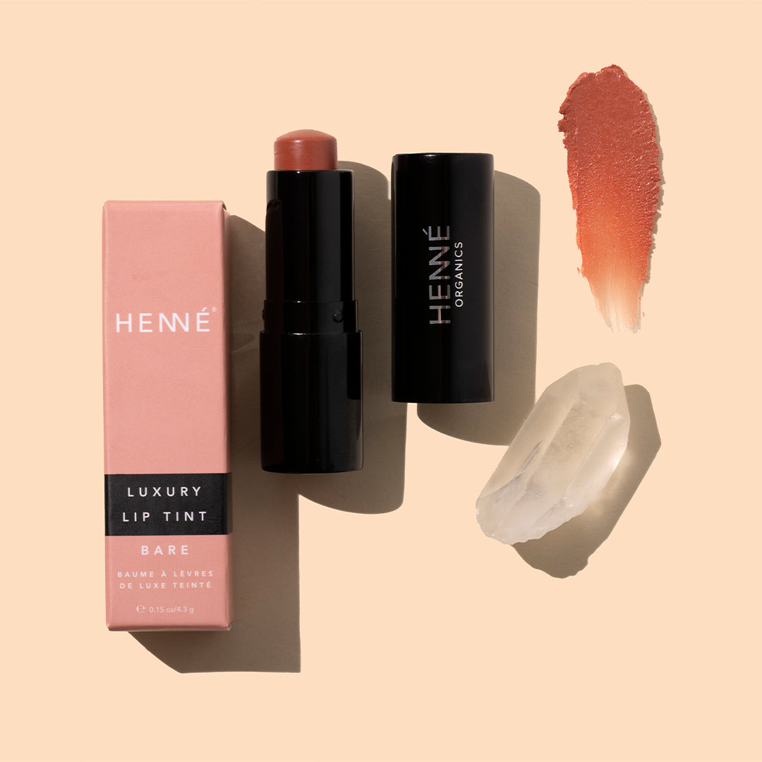 Henné | Luxury Lip Tint in Bare | Styled Image with Swatch - pink lip packaging, warm nude swatch, and crystal on a peach background