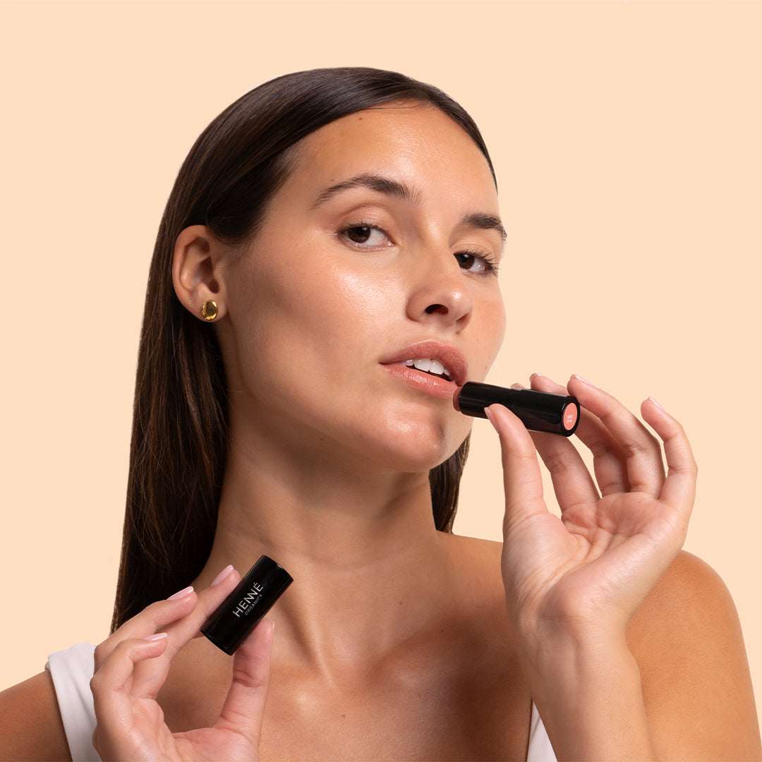 Henné Organics | Luxury Lip Tint | Model Image_Oct26 - black tube with a warm peachy-coral shade against a warm peach background
