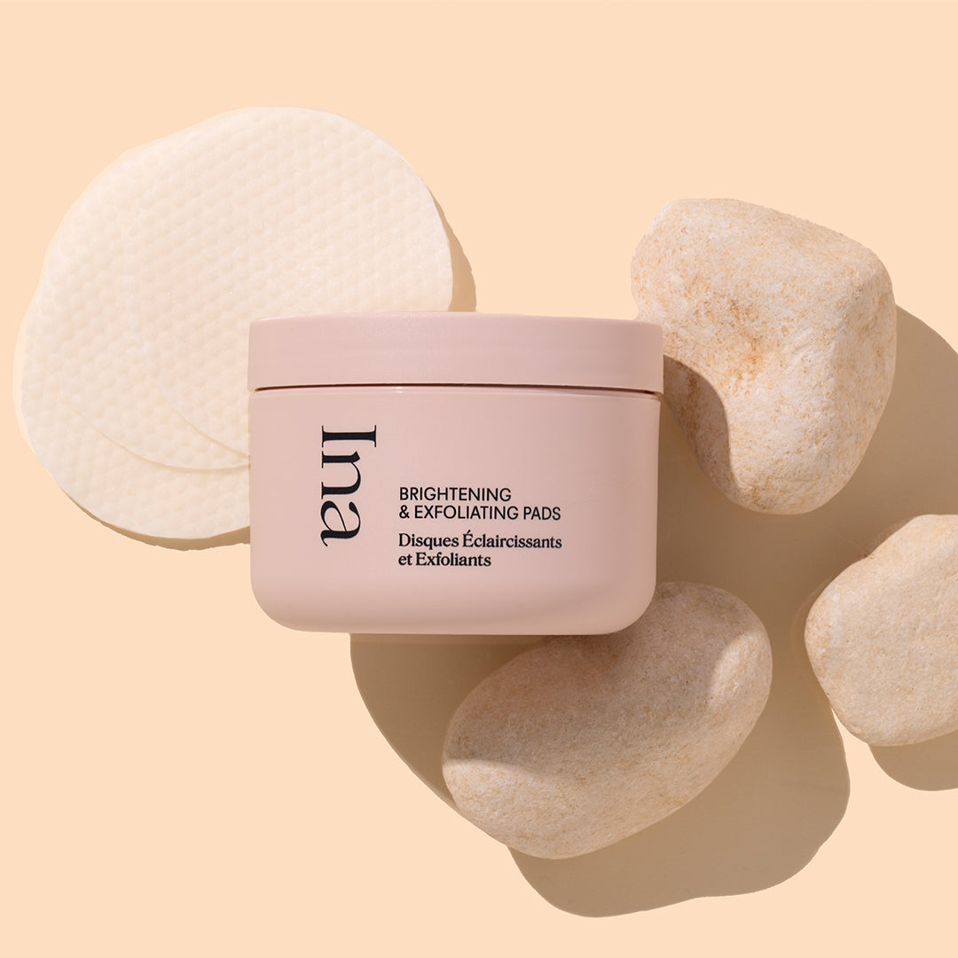 Ina | Brightening & Exfoliating Pads | Product Image - light pink jar with cotton pad and stones on a beige background