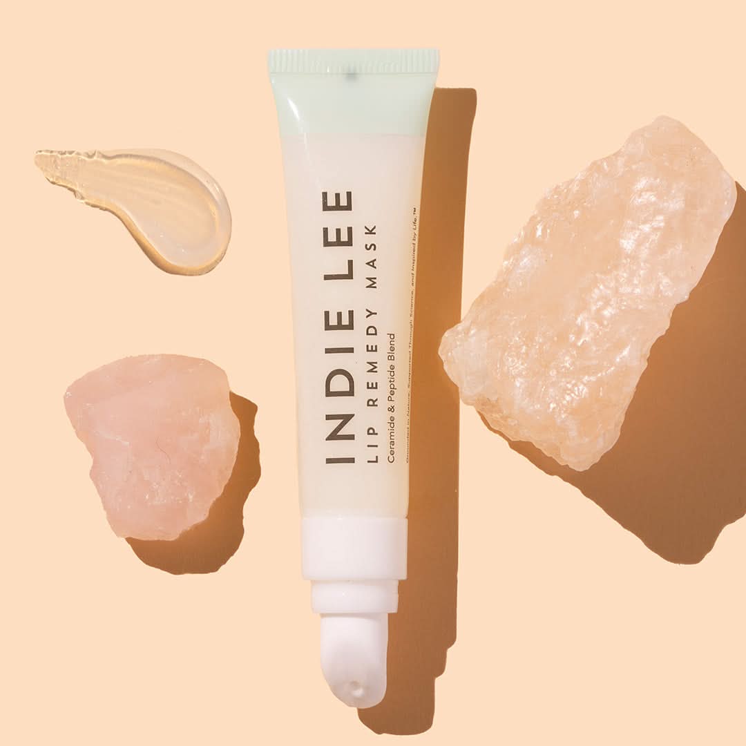 Indie Lee | Lip Remedy Mask | Styled image with swatch, white tube on peach background with beige product swatch