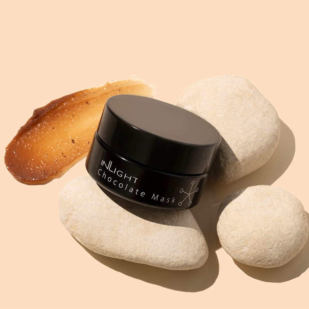 Inlight | Chocolate Mask | Model Image_Oct26 - black jar with a caramel-brown product swatch and cream-colored stones on a peach background