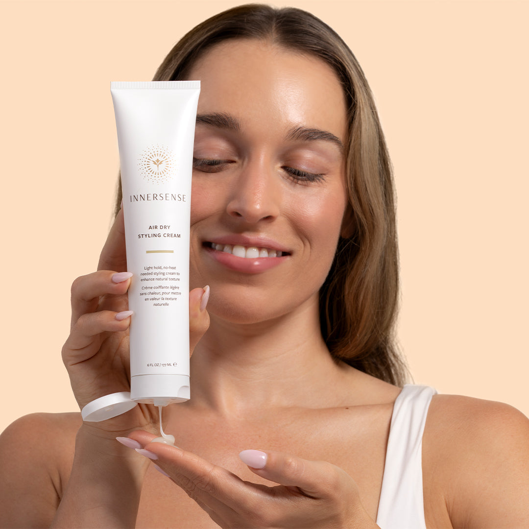 Innersense Organic Beauty | Air Dry Styling Cream | Model ImageA_Aug26 -  model dispensing cream from a white tube into her palm against a light beige background