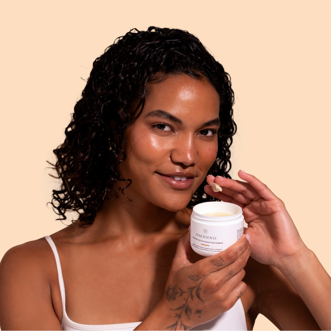 Innersense Organic Beauty | Inner Reflection Sculpting Pomade | Model Image_Jul26 - model holding jar with a small amount of pomade on fingertip against a beige background