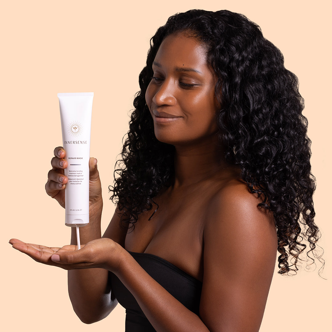 Innersense Organic Beauty | Overnight Repair Mask | Model Image - model dispensing mask into her hand while holding the tube against a soft beige background