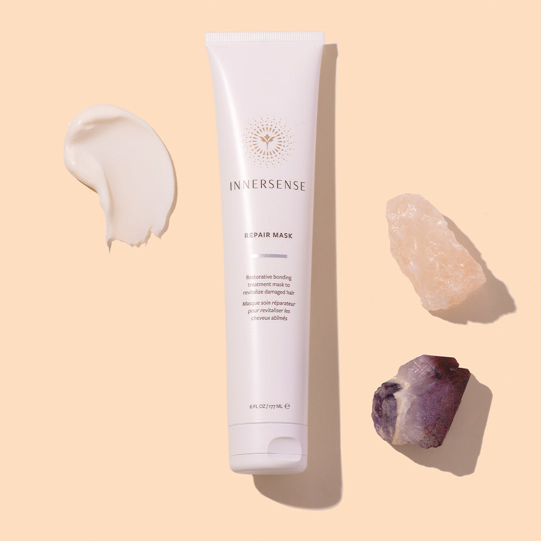 Innersense Organic Beauty | Repair Mask | Styled Image with Swatch_Aug26 - white tube with a cream swatch and crystal accents on a beige background