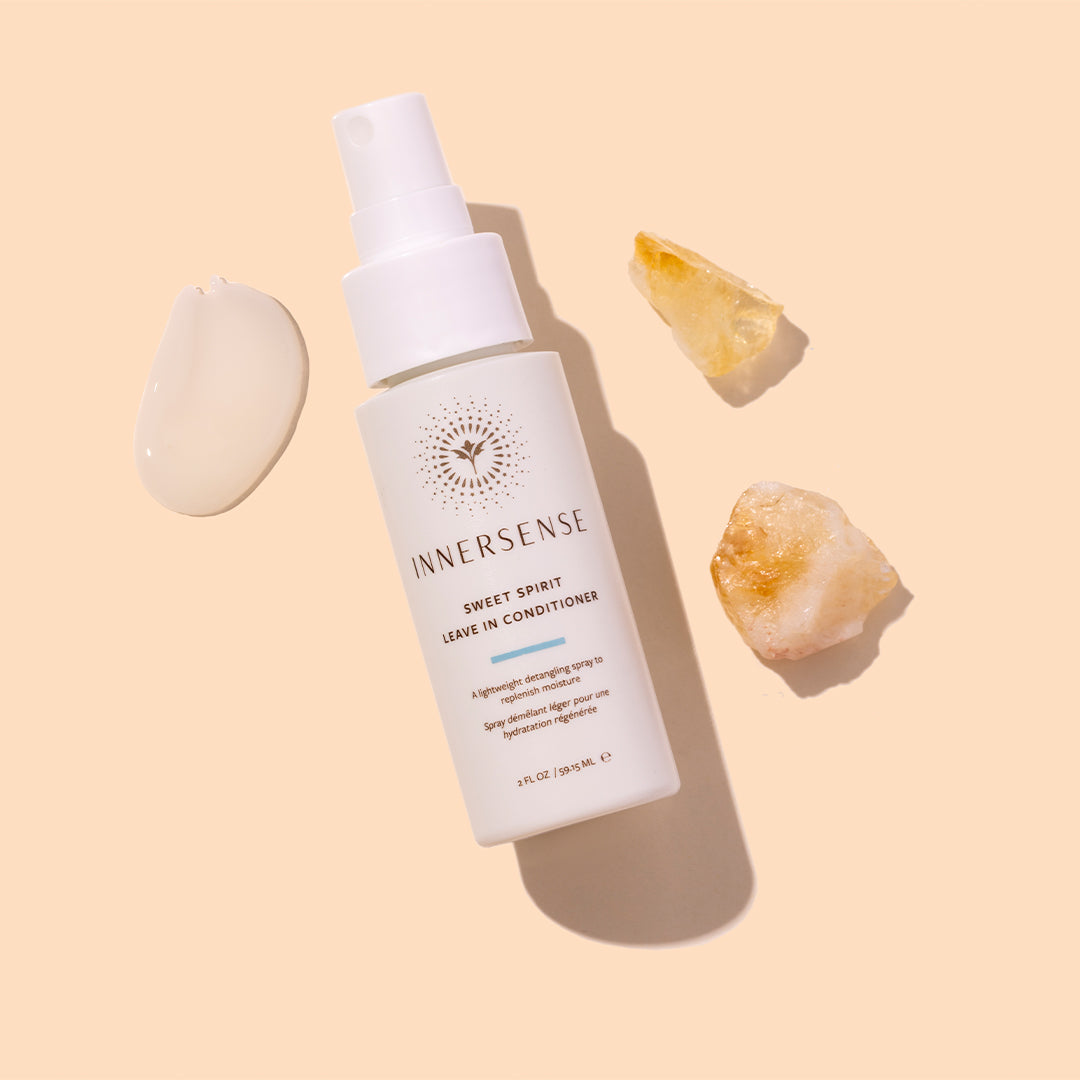 Innersense Organic Beauty | Sweet Spirit Leave-In Conditioner | Styled Image with Swatch_Aug26 - spray bottle with a cream swatch and crystal accents on a beige background