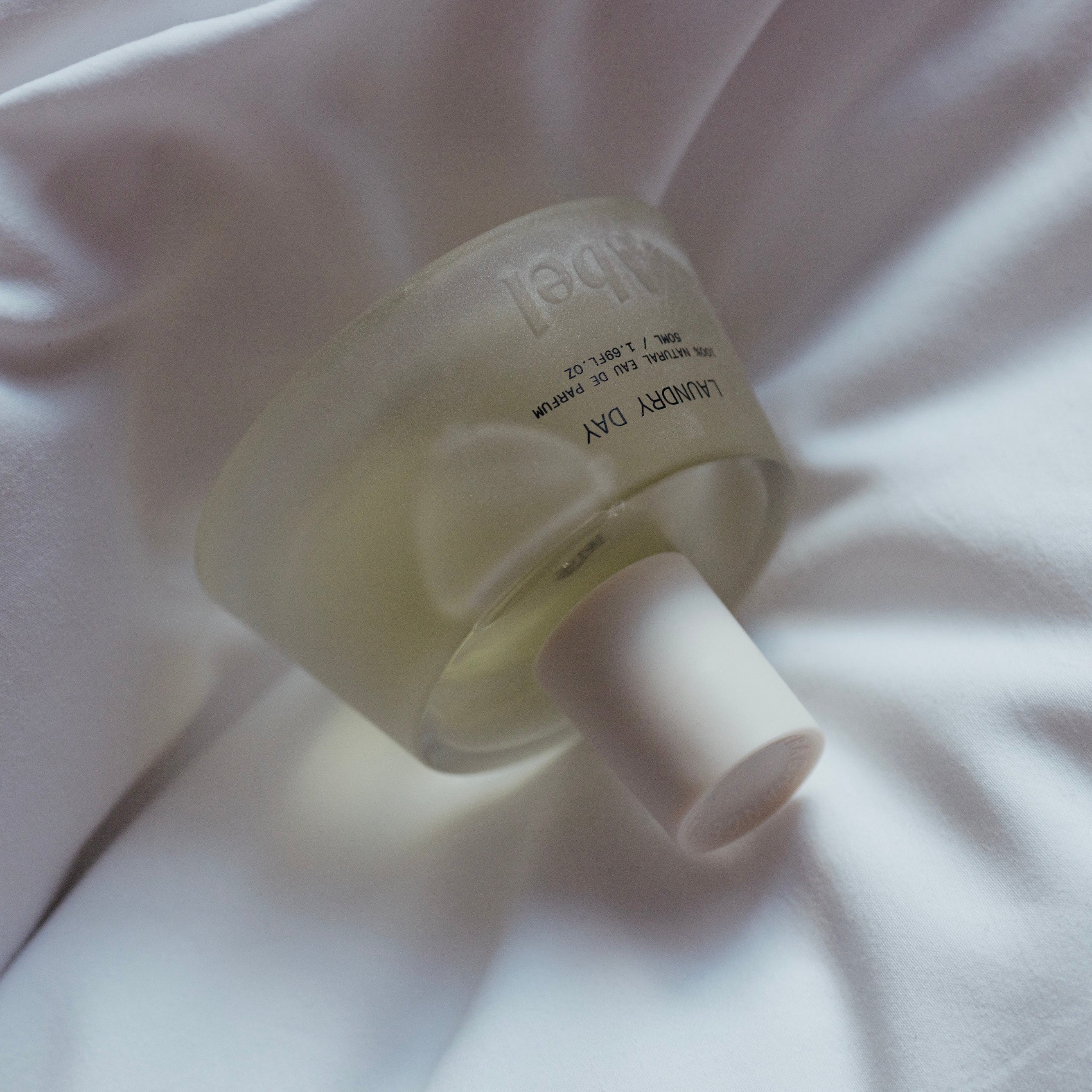 Abel | Laundry Day Eau De Parfum | Styled image | Glass perfume bottle with white top on white bedding