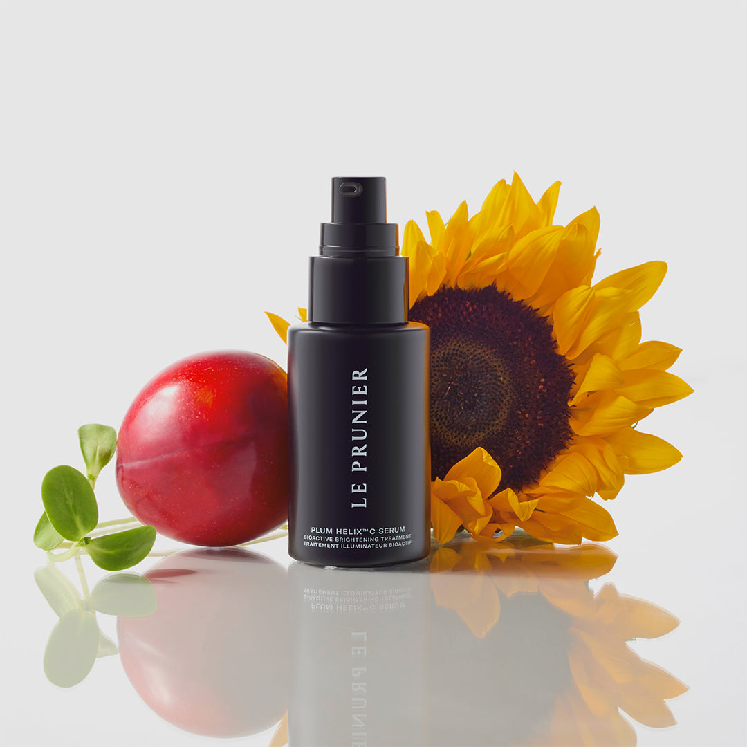 Le Prunier | Plum Helix C Serum | Lifestyle Image - black pump bottle displayed with a red plum, sunflower, and green leaves