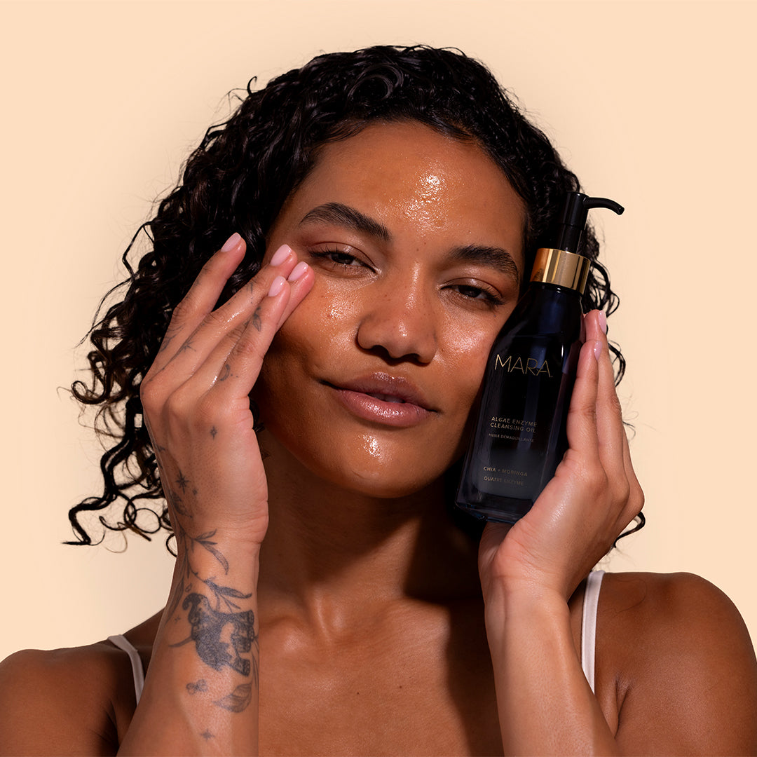 MARA | Algae Enzyme Cleansing Oil | Model Image_Jul26 - model with glowing skin holding the deep blue bottle while gently touching the face