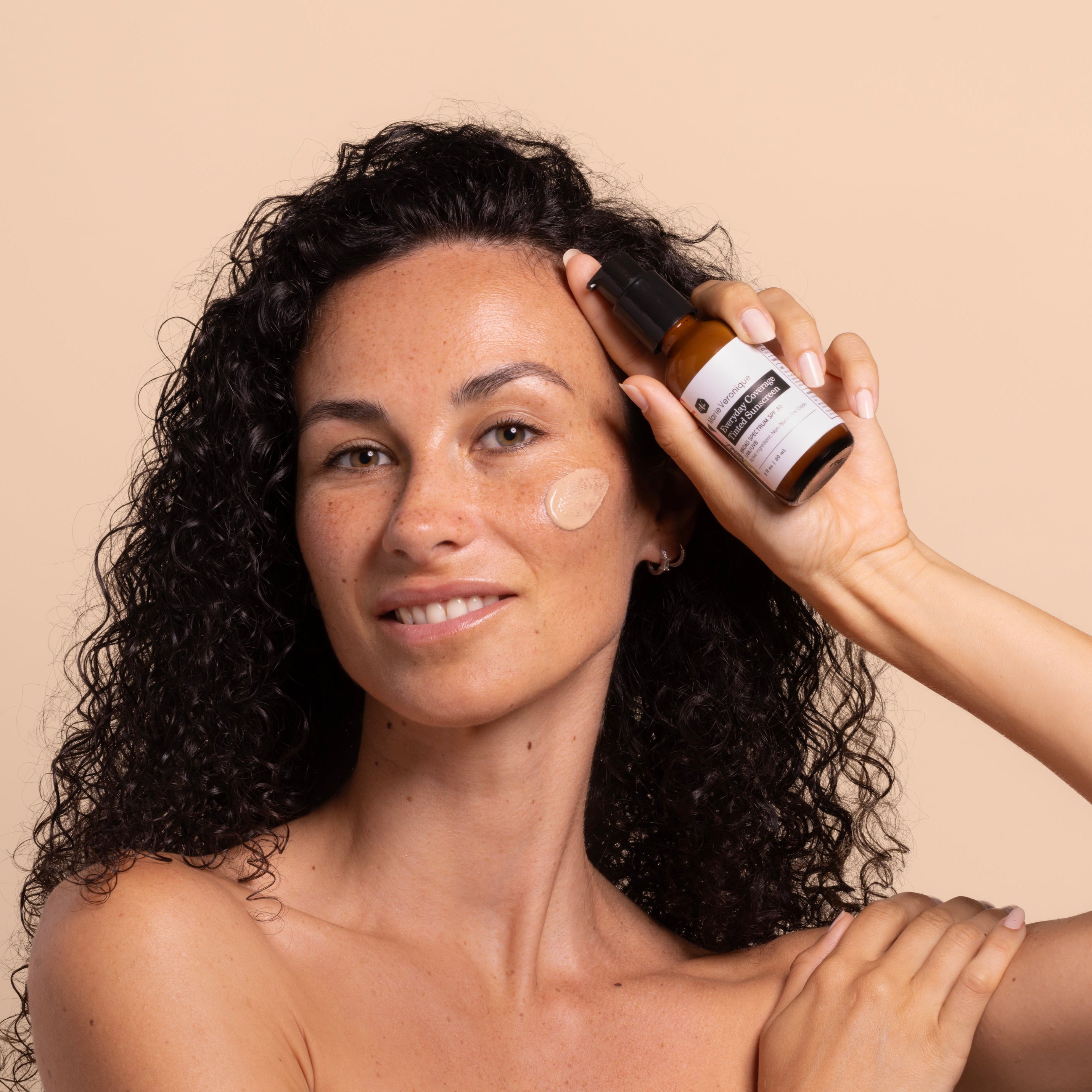 Woman applying Marie Veronique Everyday Coverage SPF  to her face with a beige background