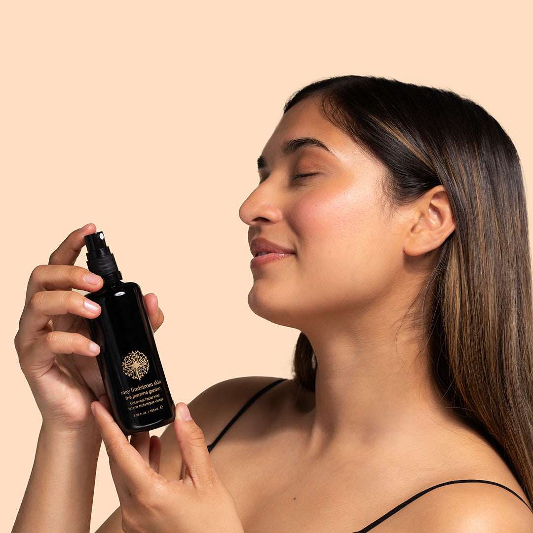May Lindstrom Skin | The Jasmine Garden | Model Image - facial mist being held and applied by a model against a peach background