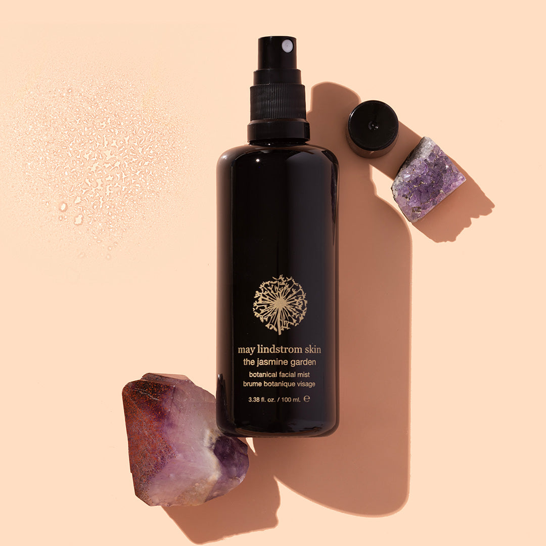May Lindstrom Skin | The Jasmine Garden | Styled Image - black spray bottle with amethyst crystals and a mist swatch on a peach background