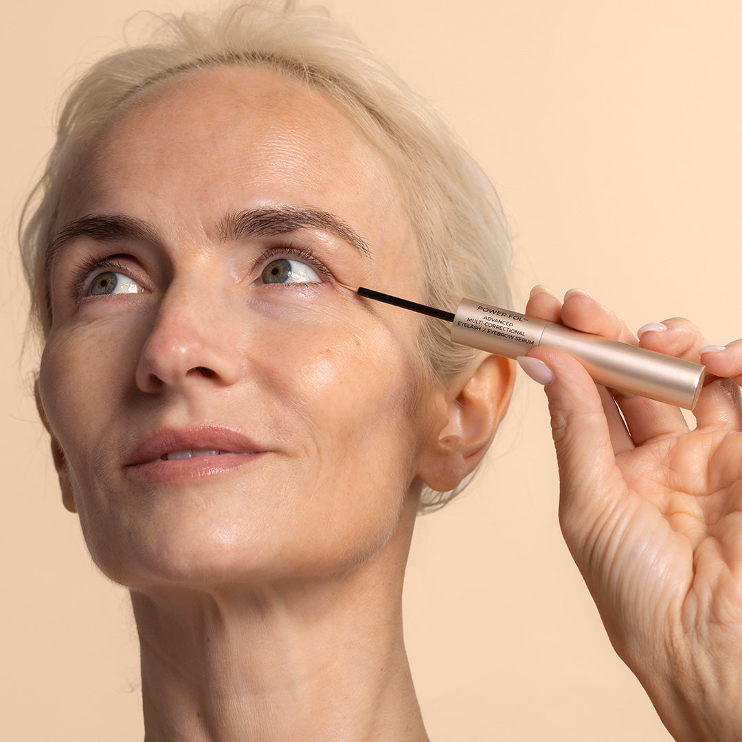 Maya Chia | Power Fol Eyelash & Eyebrow Serum | Model Image | model applying thin eyelash applicator to lash line, model against peach background