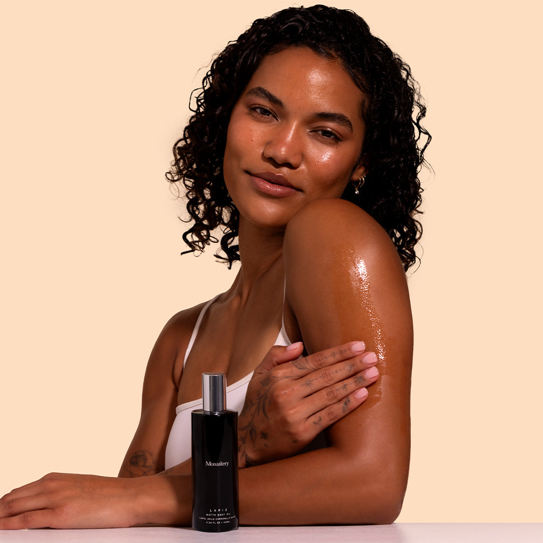 Monastery | Lapiz Matte Body Oil | Model Image_Jul26 - model applying  body oil to the upper arm with the bottle displayed in the foreground