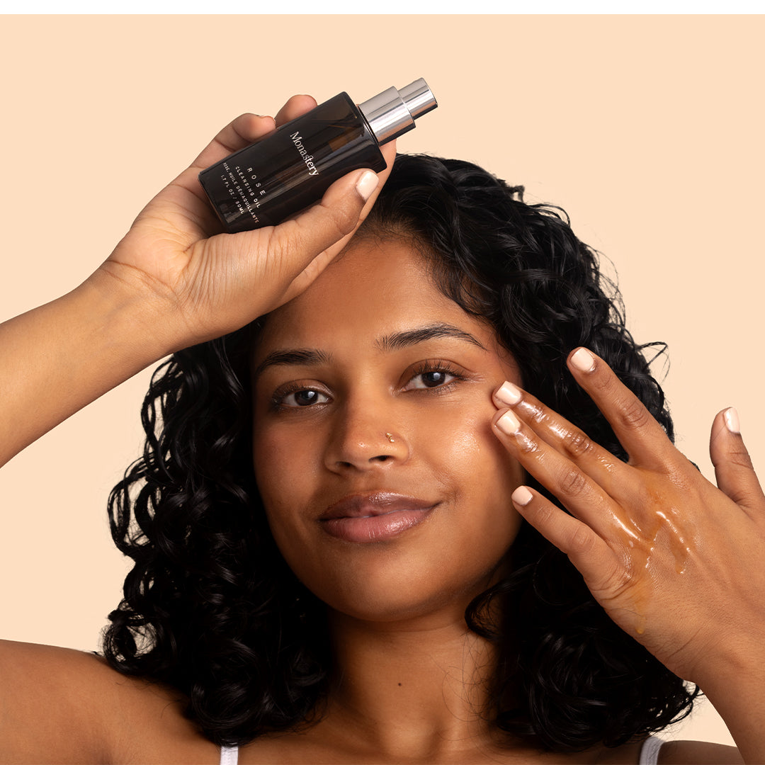 Monastery | Rose Cleansing Oil | Model Image - person applying oil while holding a dark amber bottle with pump dispenser
