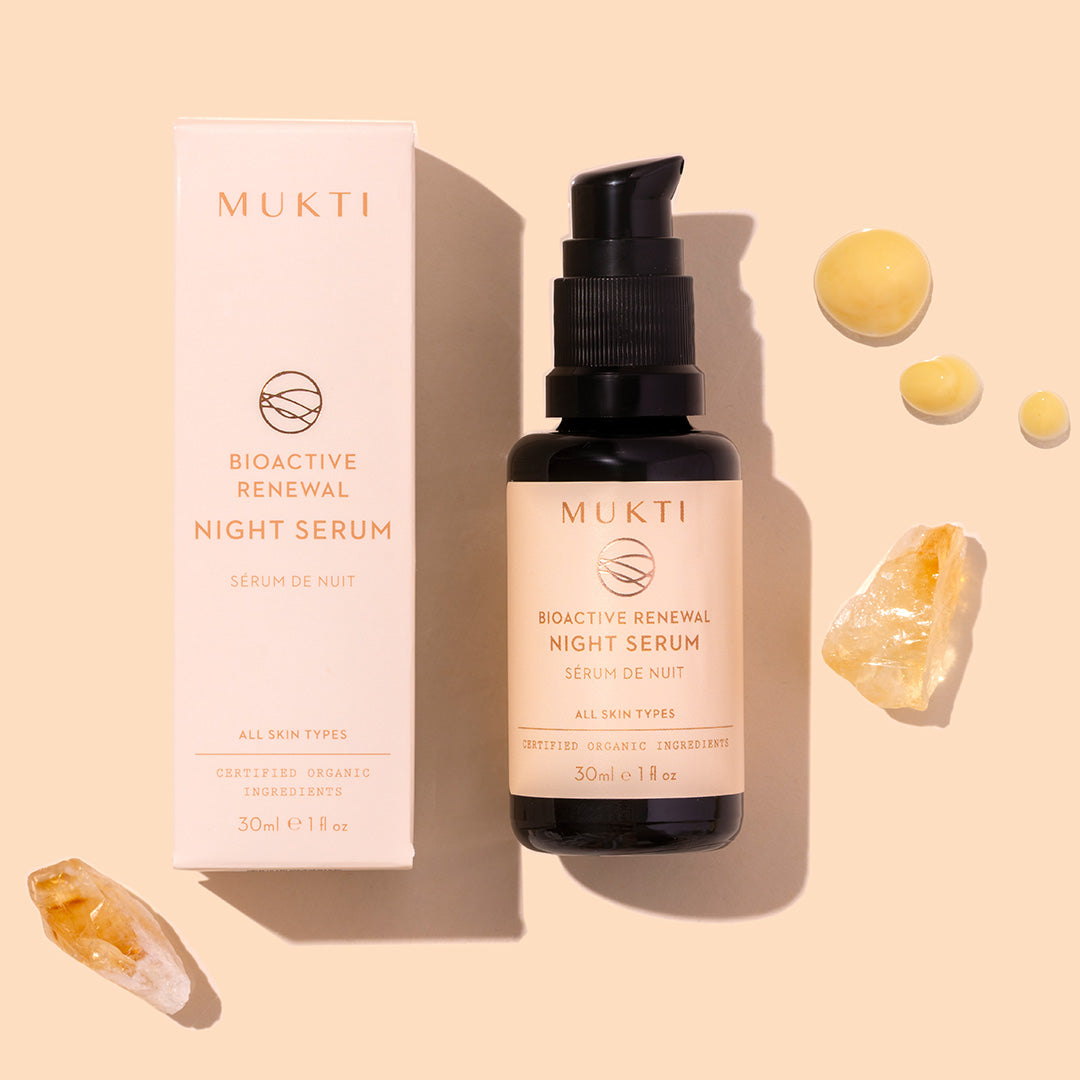 Mukti | Bioactive Renewal Night Serum | Styled image with swatch | dark bottle on peach background with yellow product swatch droplets