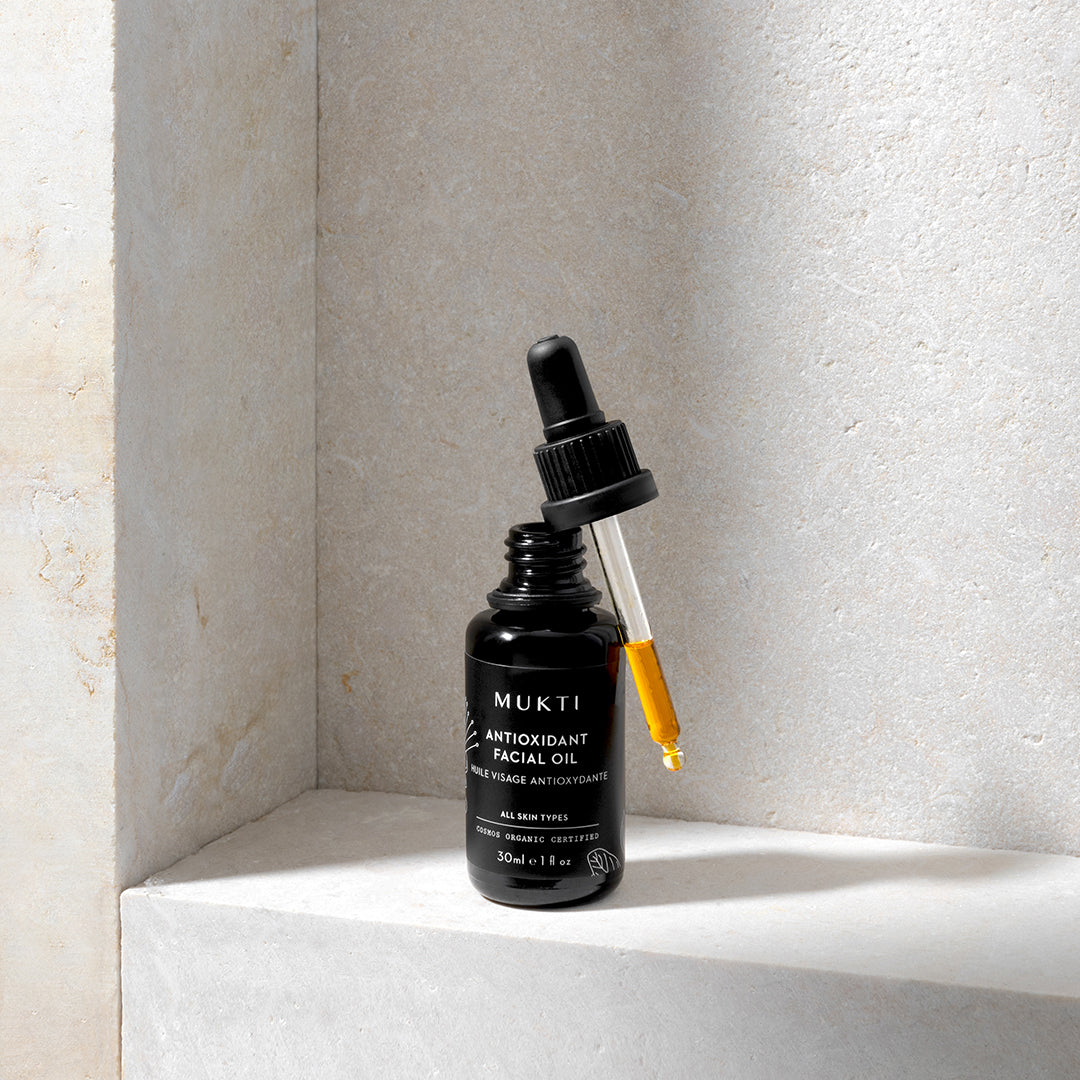Mukti Organics | Antioxidant Facial Oil | Lifestyle Image - black dropper showing golden oil on a stone ledge
