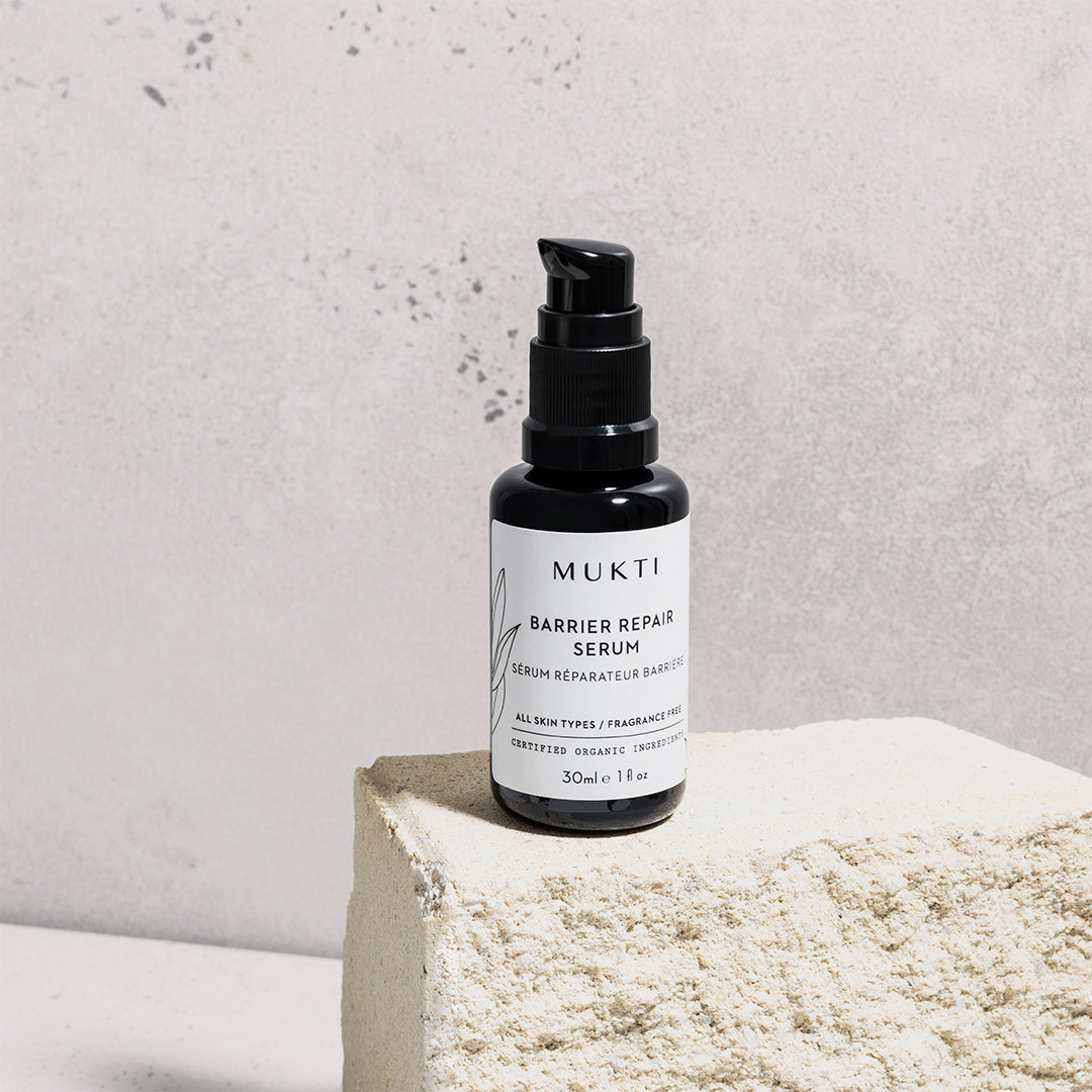 Mukti Organics | Barrier Repair Serum | Lifestyle Image - black pump bottle displayed on a textured stone pedestal
