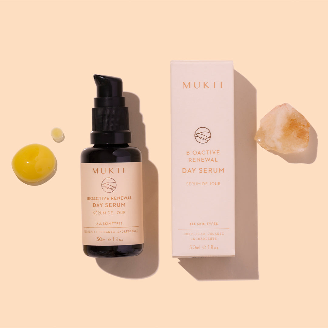 Mukti Organics | Bioactive Renewal Day Serum | Styled Image with Swatch_Aug26 - serum bottle and box displayed with golden serum droplets and a crystal on a light beige background