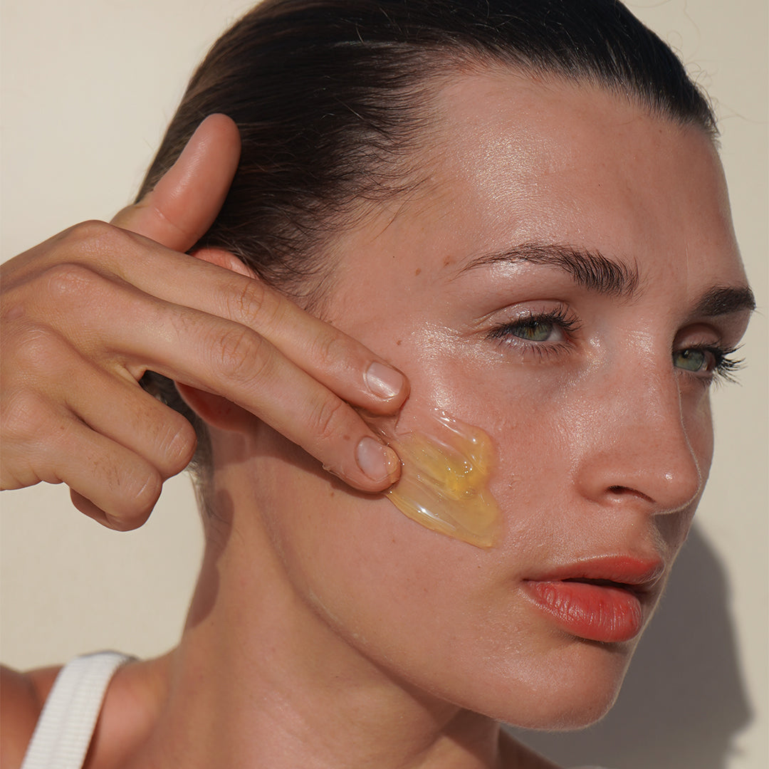 Mukti Organics | Gentle Melt Cleansing Balm | Model Image - model applying a golden cleansing balm to her cheek