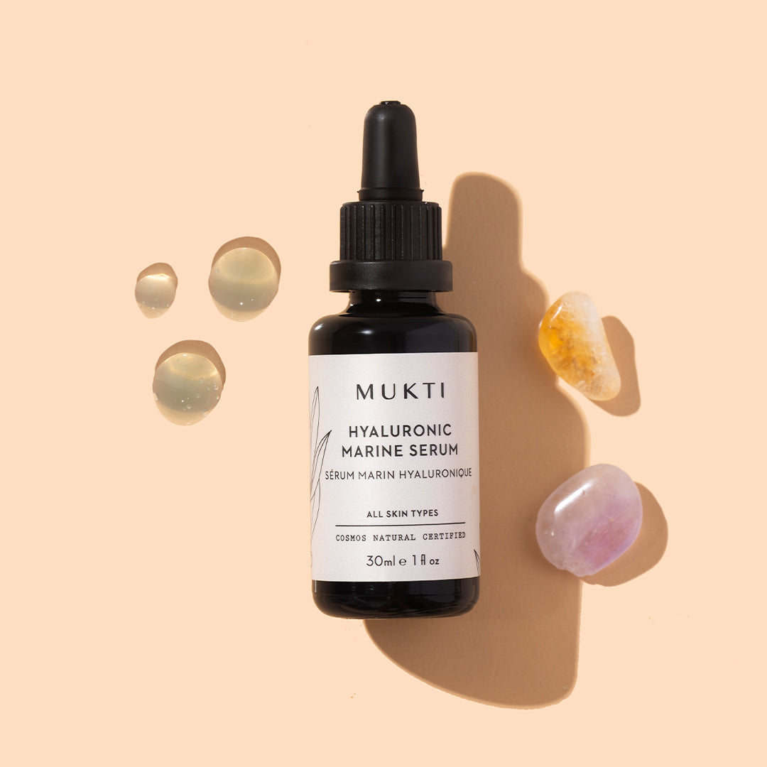 Mukti Organics | Hyaluronic Marine Serum | Styled Image with Swatch - dropper bottle styled with serum droplets and crystals on a beige background